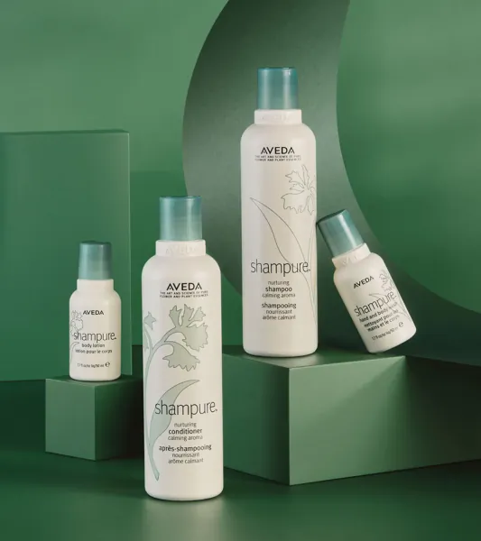 Aveda Shampure shampoo, conditioner, and styling products on green display with floral motifs.