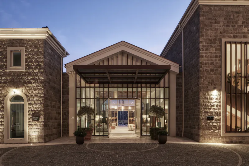The Chedi Luštica Bay Montenegro: stone hotel entrance with glass doors, potted plants, and courtyard at dusk