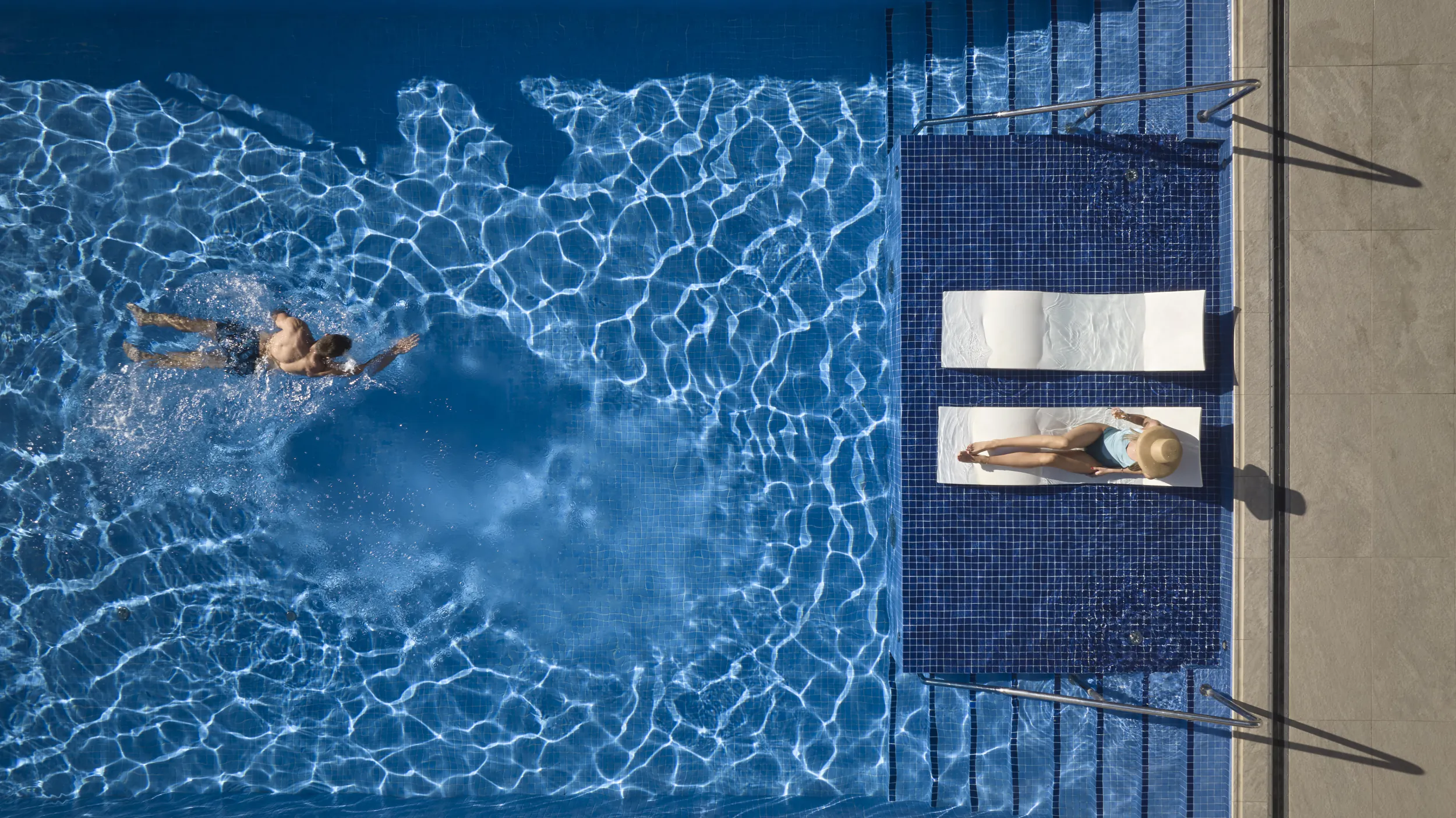 Aerial view of infinity pool at The Chedi Montenegro: person swimming, another lounging on chaise with hat.