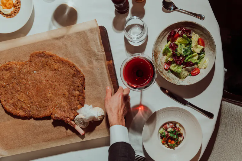 Elegant table at Sartoria: oversized breaded veal chop with bone and cream, red wine, salads on white plates.