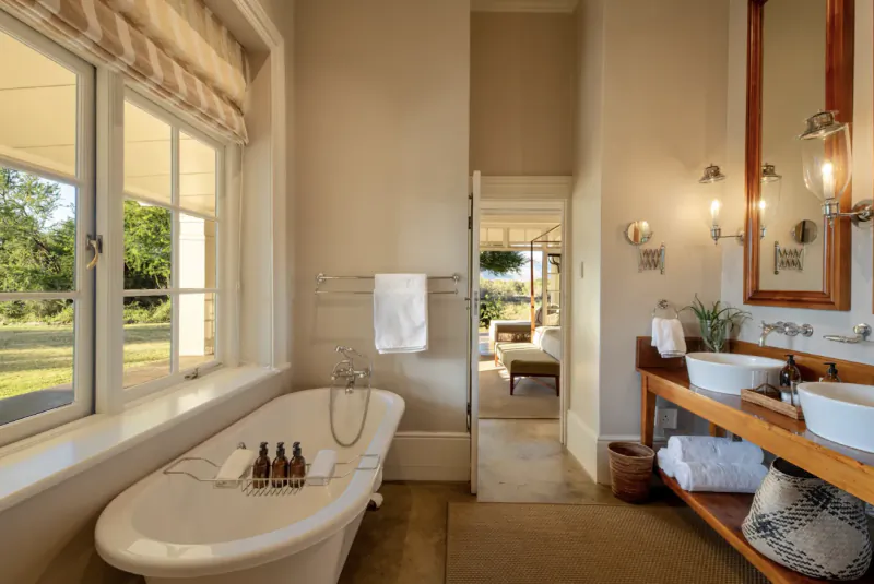 Elegant bathroom in Samara Karoo Safari Villa with clawfoot tub, double sinks, towels, and garden view