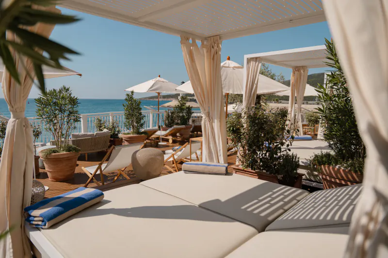 Luxury poolside daybeds with beige curtains and umbrellas at The Chedi Luštica Bay, overlooking Adriatic Sea.