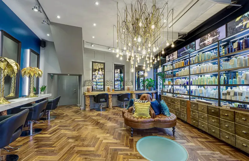 Modern Edward James London hair salon interior with blue walls, wooden floors, stylist chairs, product shelves, and chandelier.