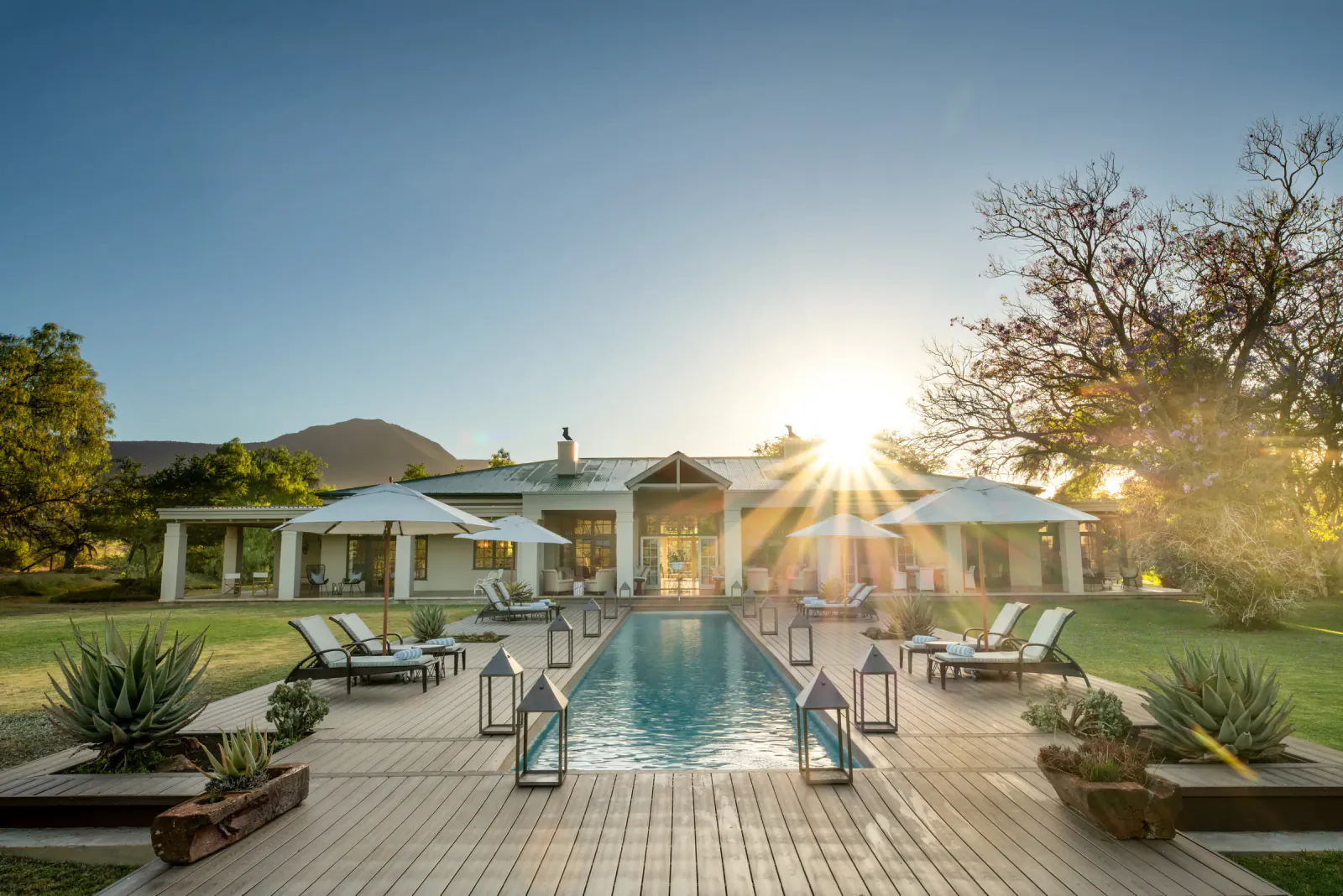 Samara Karoo Safari Villa: refined private retreat with long pool, loungers, lanterns, agaves, trees, and mountains at sunset