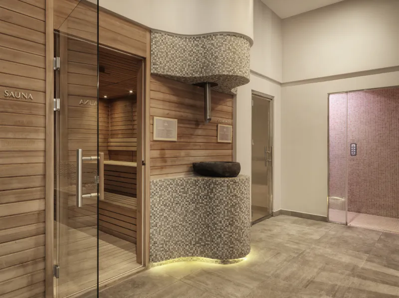 Modern spa at The Chedi Luštica Bay: wooden sauna with glass door, curved stone wall, black basin, pink shower room.