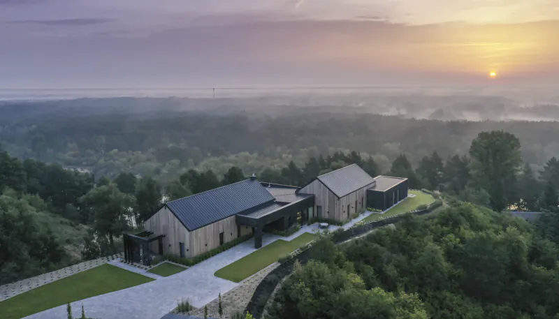 Aerial view of Vilea – Adrian modern barn-style buildings on a lush green hillside at sunset with expansive valley vista