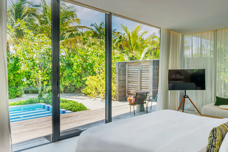 Luxury Maldives villa bedroom with large windows overlooking lush tropical garden and blue plunge pool
