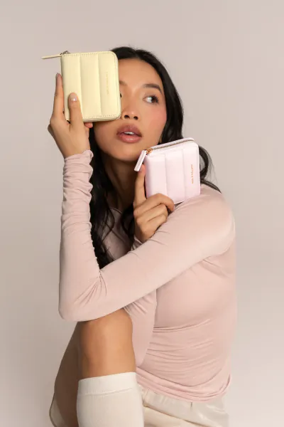 Asian woman in pink top holding yellow and pink puffy wallets, soft cloud-like design, seated pose