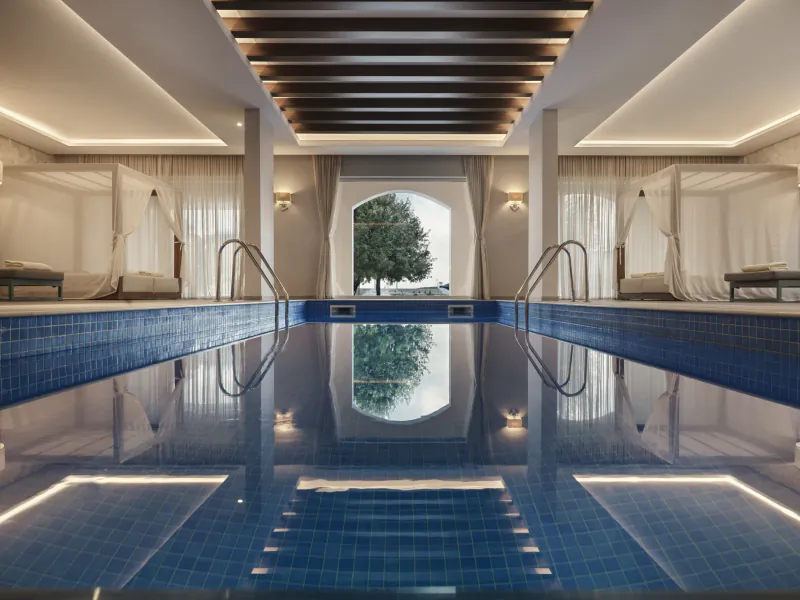 Luxurious indoor pool at The Chedi Luštica Bay, Montenegro, with arched window to tree, daybeds, warm lighting.