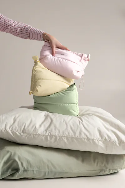 Hand holding pink puffy pillow atop stacked yellow, green, and white pillows from Kapten & Son Cloud Club