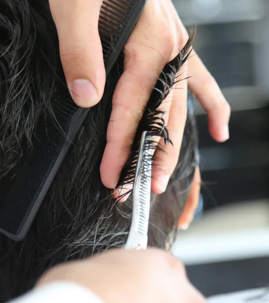 Close-up of stylist combing and trimming a client's thick black hair in salon