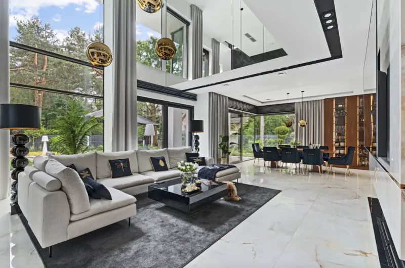 Spacious modern living room in Vilea – Adrian with white sofas, black coffee table, gold pendant lights, dining area, large windows overlooking trees
