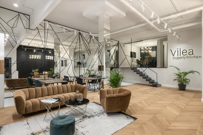 Modern Vilea Property Boutique office with geometric metal framework, beige sofas, plants, and staircase.