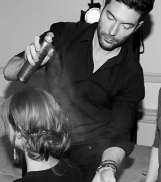 Handsome male stylist spraying hairspray on woman's elegant updo at Edward James London salon