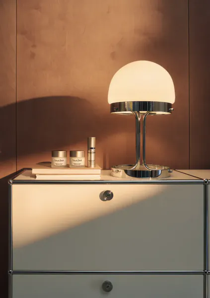 White Vitra sideboard with chrome mushroom lamp, skincare jars, and bottle on terracotta wall in soft light.