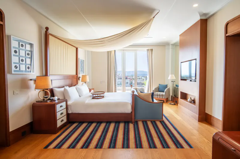 Luxurious hotel bedroom with canopy bed, striped rug, city view windows, and wooden accents