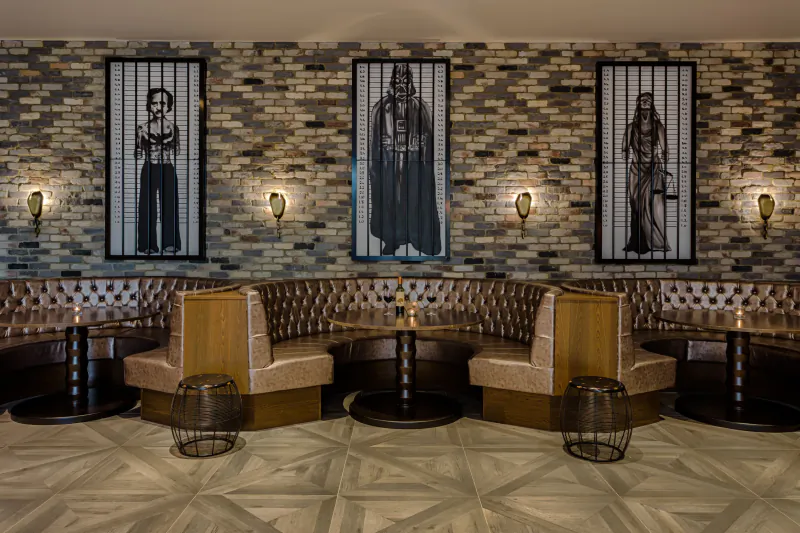 Courthouse Shoreditch interior: brick wall with three tall black-and-white figure portraits, curved tan leather booths, wall lamps, round tables.