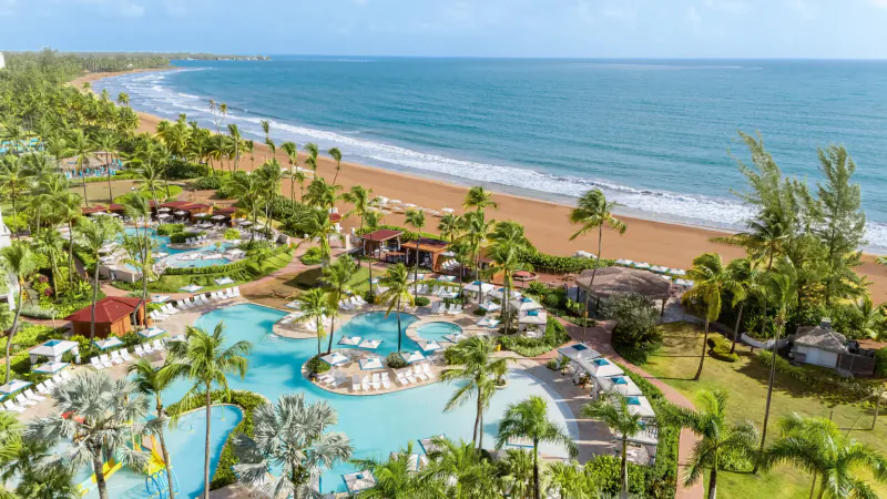 Aerial view of Wyndham Puerto Rico resort with turquoise pools, palm trees, and sandy beach on the ocean.