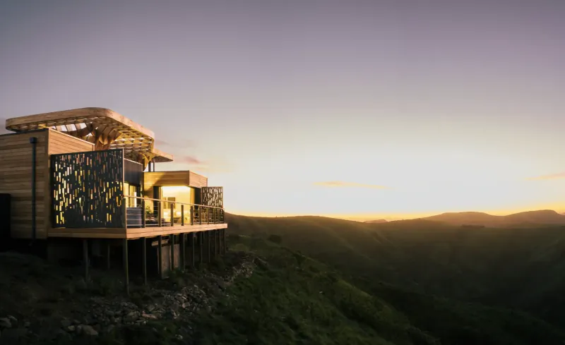 Modern wooden Hiddn lodge elevated on stilts over lush green Addo mountains at sunset