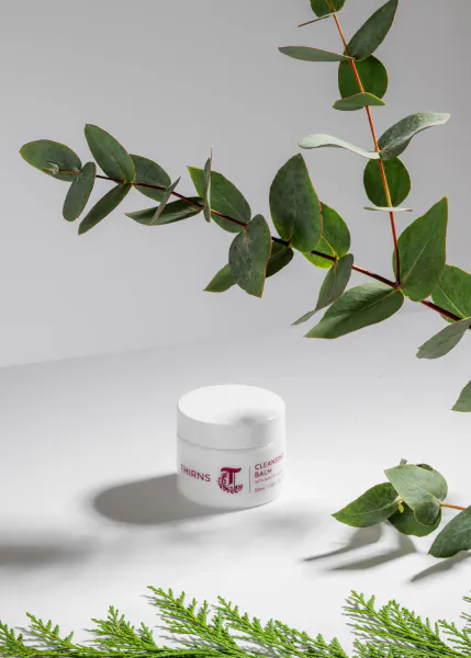 White jar of Thirns cream on white surface, surrounded by eucalyptus and fir branches
