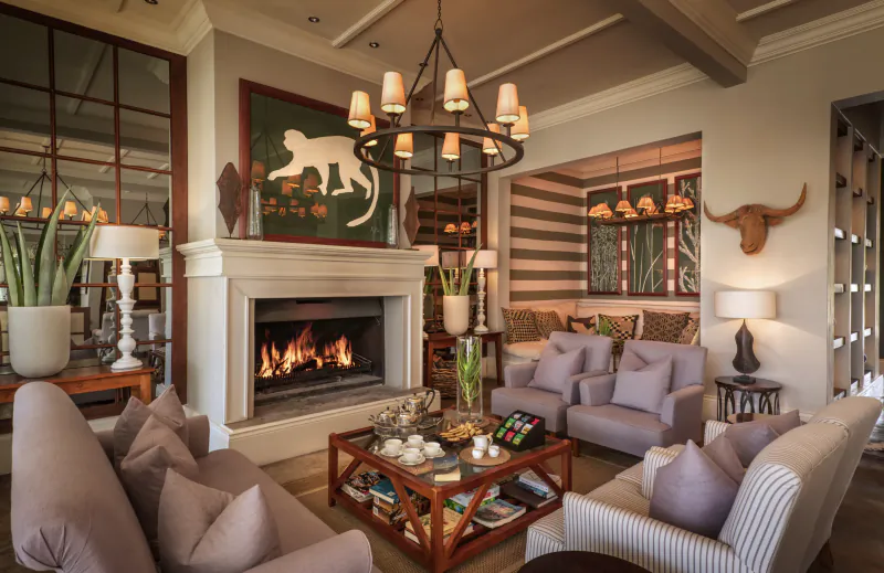 Cozy lounge in Samsara Karoo Safari Villa with lit fireplace, monkey art, longhorn skull, plush sofas, and tea table.