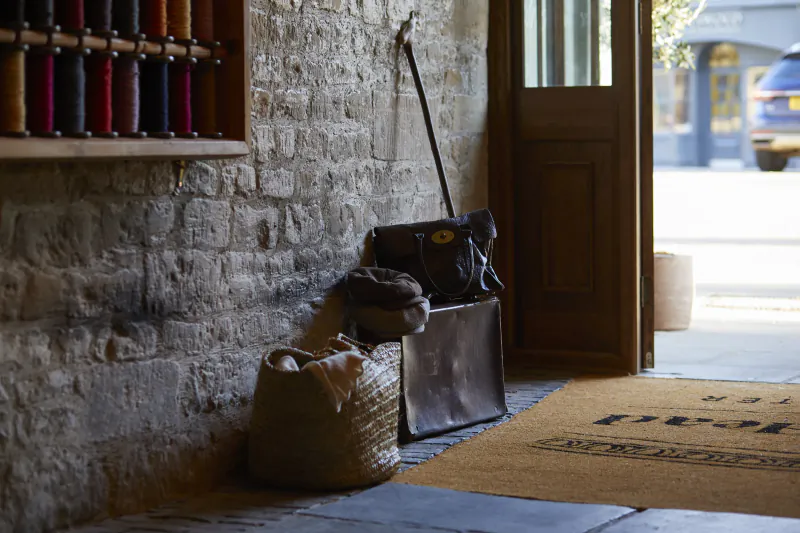 Kings Head Cirencester entrance: stone wall with yarn shelves, broom, bags, basket on mat