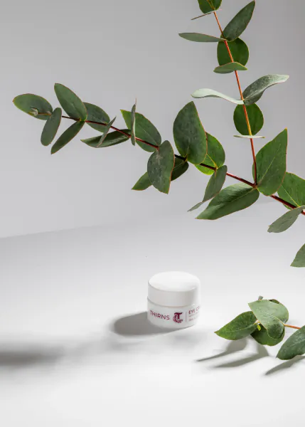 White jar of Thirns cream on white surface, surrounded by eucalyptus leaves