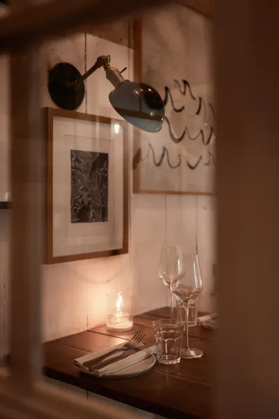 Cozy restaurant table with wine glasses, candlelight, utensils, and framed art viewed through window frame