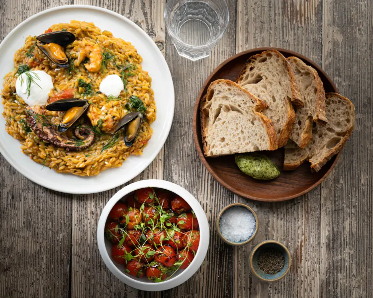 Saffron risotto with mussels, octopus, burrata, cherry tomatoes, bread, and seasonings on wooden table