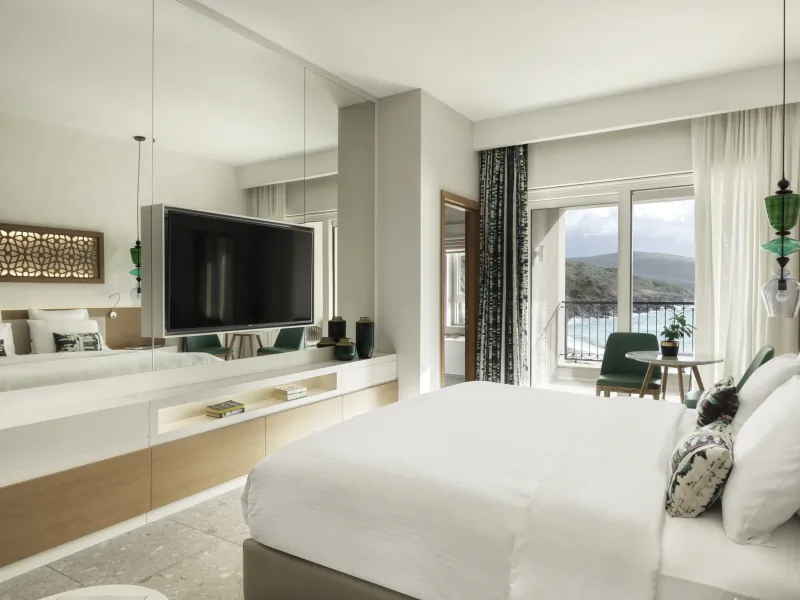 Spacious hotel room at The Chedi Luštica Bay with king bed, TV, balcony view of sea and mountains.