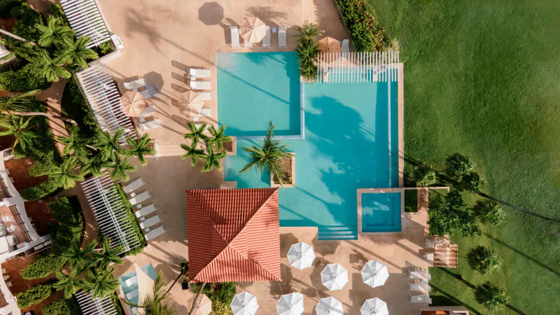 Aerial view of Wyndham Puerto Rico's turquoise pool with palm trees, lounge chairs, red-roofed cabana, and green lawn.