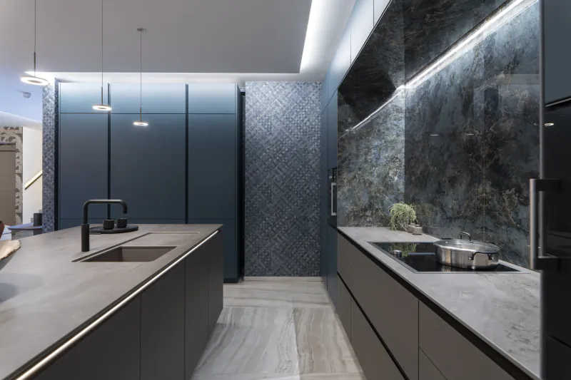 Modern luxury kitchen with dark blue cabinets, marble backsplash, and large central island with black sink and pendant lights
