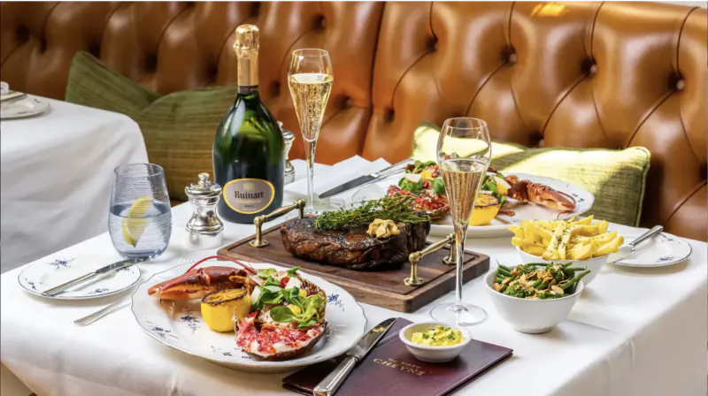 Luxurious restaurant table with Moët & Chandon champagne, grilled steak, lobster, fries, and sides on elegant white plates.