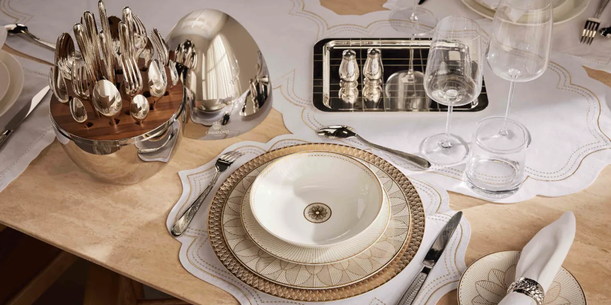 Elegant Limoges porcelain table setting with white bowl, gold-rimmed plates, silver utensils, and wooden cutlery holder on white tablecloth.