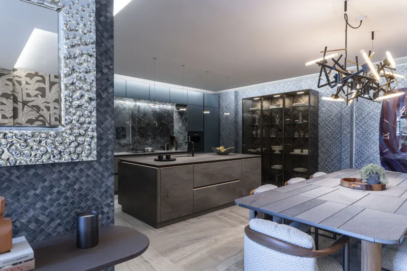 Modern kitchen and dining area with dark cabinetry, marble backsplash, ornate mirror, and sculptural chandelier over a dining table