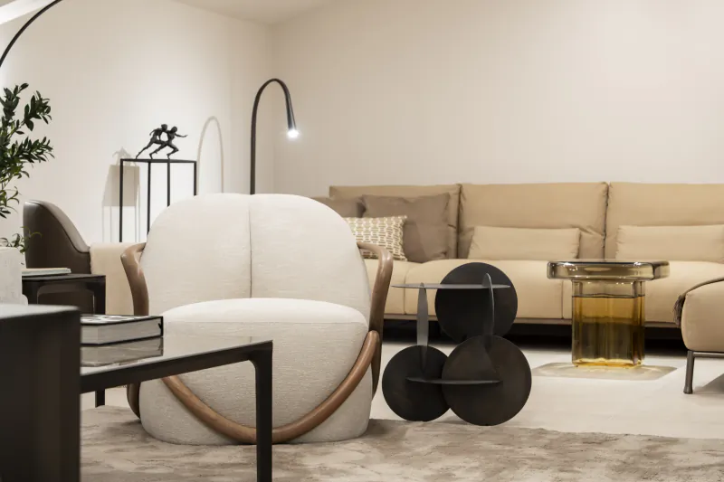 Modern living room with white boucle armchair, beige sofa, sculptural black side tables and amber glass coffee table in a minimalist showroom