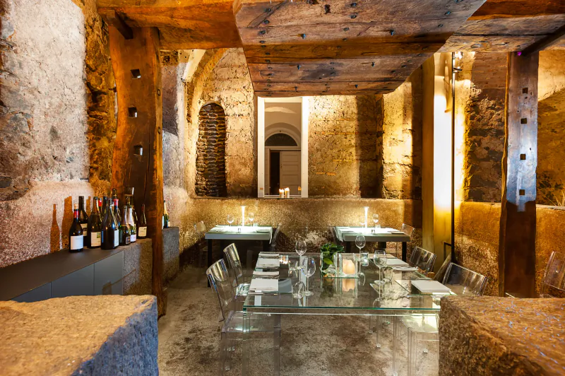 Elegant dining room in rustic stone vault at Zash Country Boutique Hotel, with glass tables, wine bottles, and warm lighting.