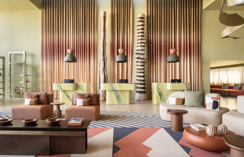 Modern hotel lobby with green marble reception desks, wooden sculptures, pendant lights, and colorful rugs in Portugal resort.