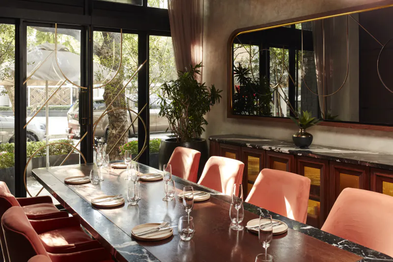 Hyde Johannesburg: Boho dining room with black marble table, pink chairs, plants, gold mirror, and city skyline view through windows.