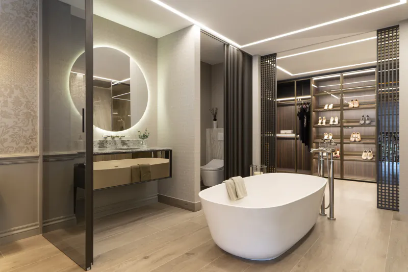 Modern luxury bathroom with freestanding white bathtub, backlit round mirror vanity, and open walk-in wardrobe with shoe display