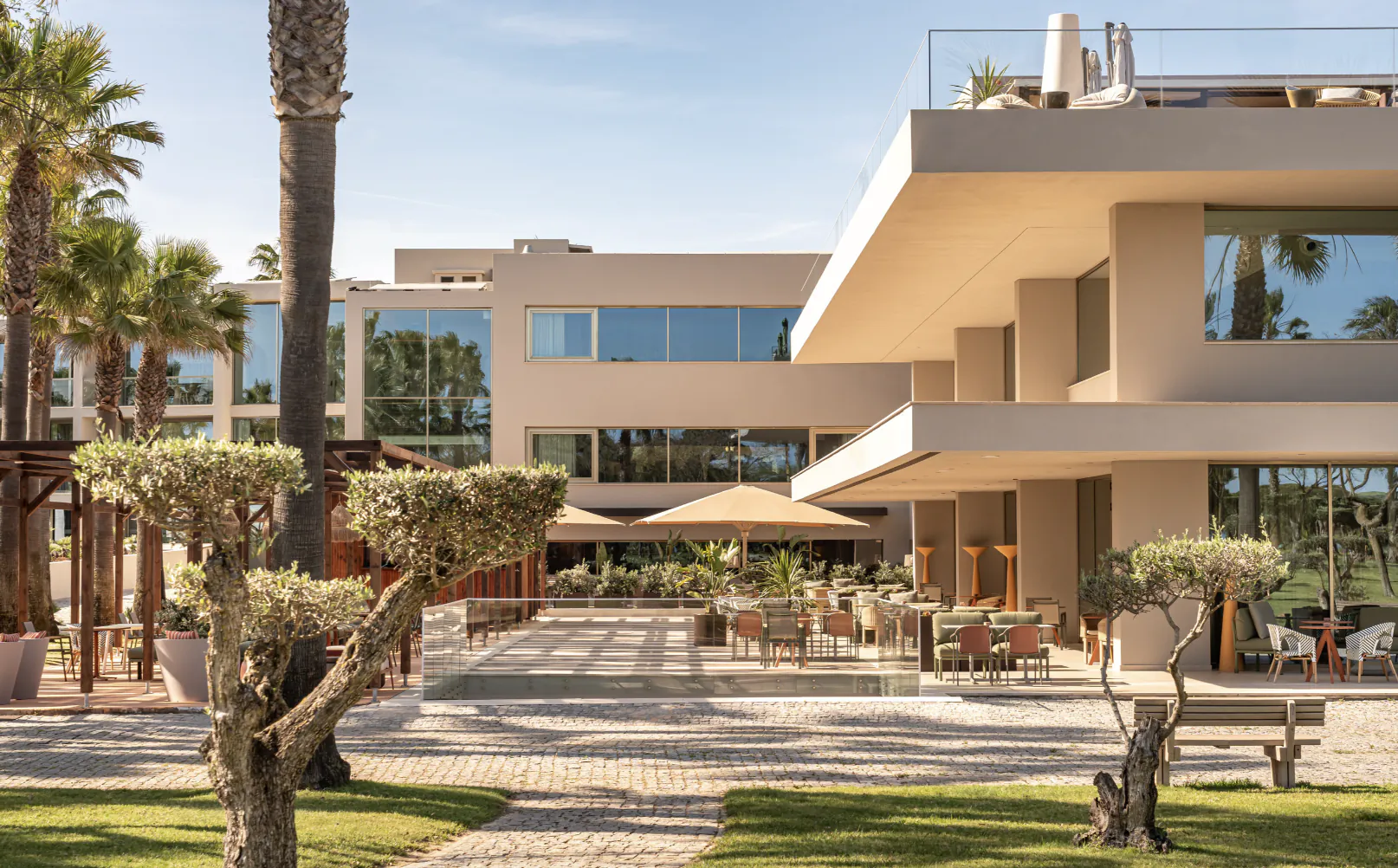 Modern luxury hotel exterior on Portugal's sunny south coast with outdoor seating, palm trees, and landscaped gardens.