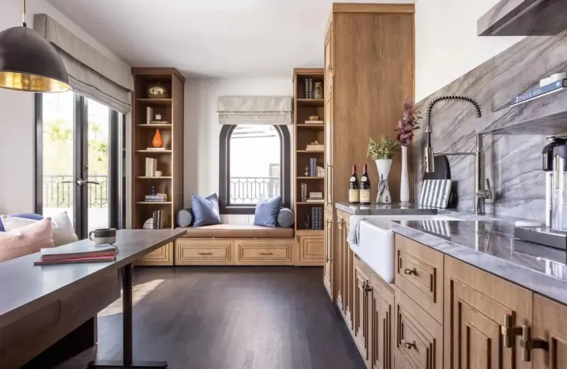 Modern kitchen with wooden cabinets, marble countertops, and a built-in window seat with blue cushions