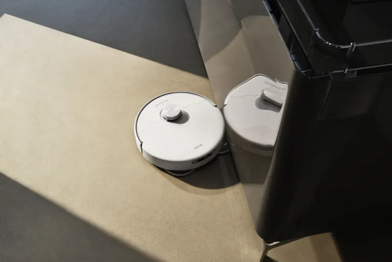 White MOVA robot vacuum docked next to its charging station on a light floor