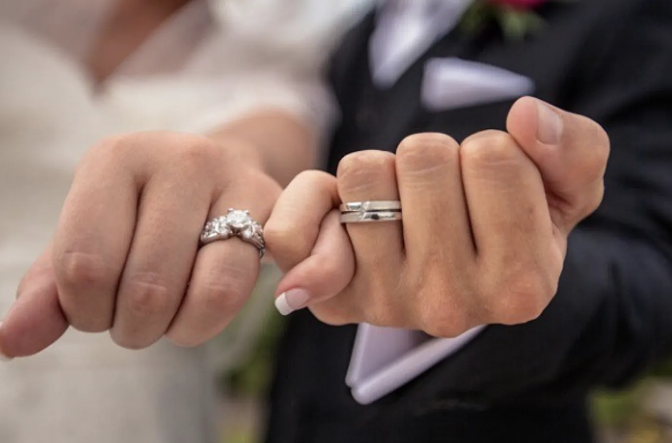 Close-up of bride and groom's hands showing wedding rings, interlocked fingers with diamond engagement ring and silver band