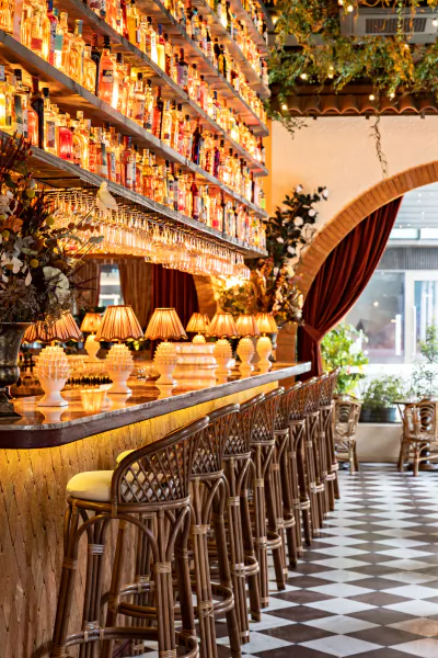 Elegant bar with rows of backlit liquor bottles, woven bar stools, and warm lighting in a stylish restaurant interior