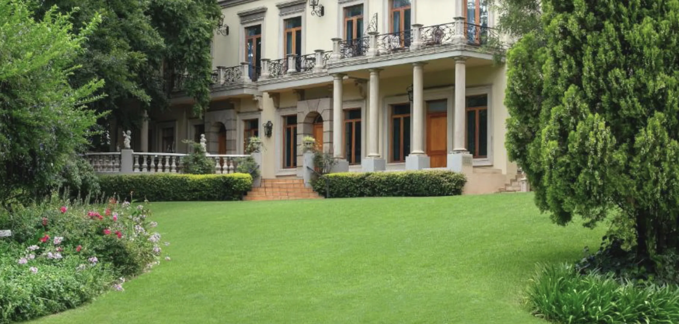 Elegant two-story Fairlawns Boutique Hotel with columns, balconies, and lush green lawn and gardens