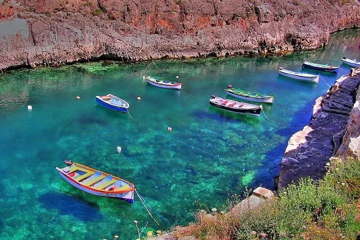 Colorful small boats floating in clear turquoise water at the base of steep rocky cliffs