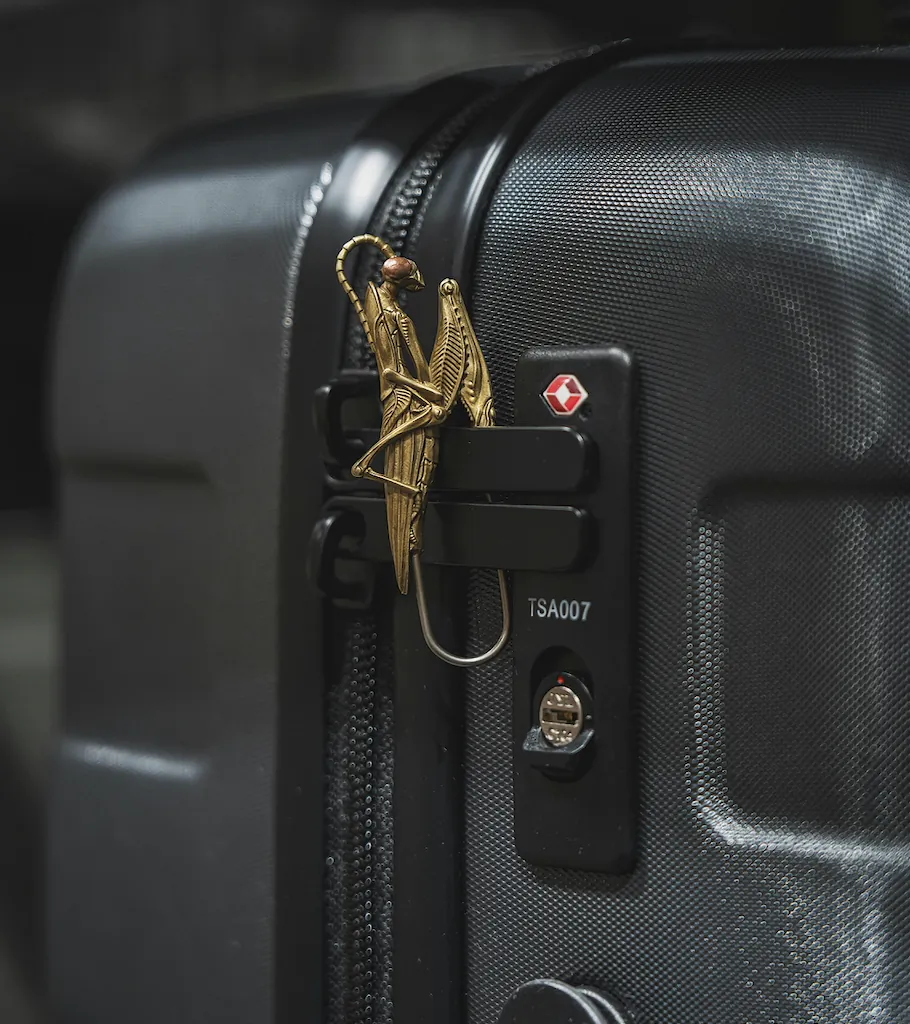 Golden grasshopper keychain on zipper and TSA007 lock of black hard-shell suitcase