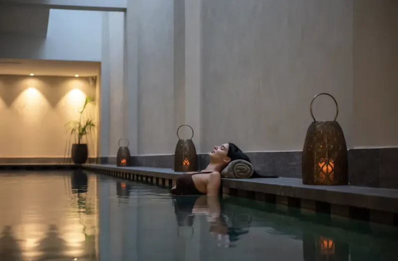 Woman relaxing in pool at Cap St Georges Hotel & Resort, reclining on edge with towel, lit by lanterns.
