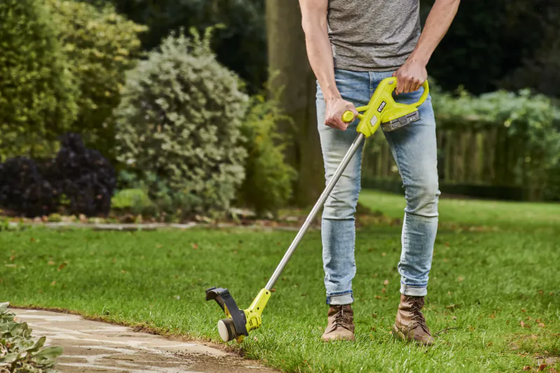 Person using a Ryobi string trimmer to edge grass along a garden path